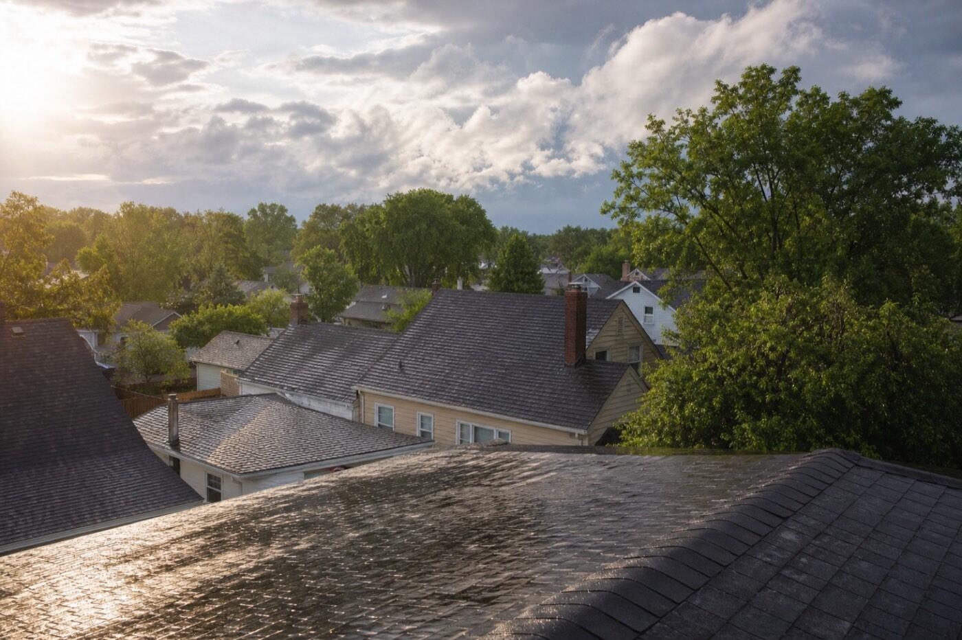 Illustrative image of wet rooftops in a residential neighborhood shining after a summer storm under clearing clouds.